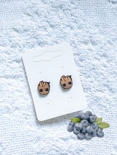 pair of earrings with baby groote face on them sitting next to some grapes