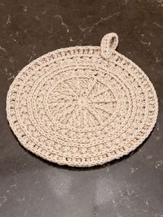 a round woven placemat on a black counter top with a white handle and loop