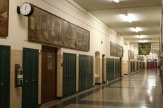 an empty hallway with several doors and pictures on the wall above them, along with a clock