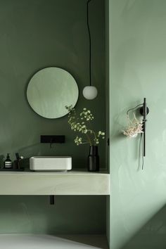 a bathroom with green walls and a white sink under a round mirror on the wall