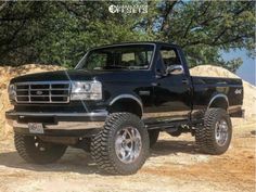 a black pickup truck parked on top of a dirt road next to trees and rocks