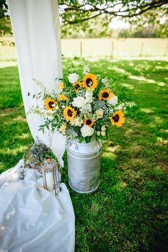 a bouquet of sunflowers sits in a bucket next to a white drape