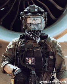 a man wearing a helmet and goggles standing in front of a jet engine