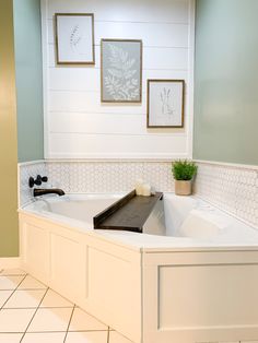 a bathroom with a white bath tub sitting next to a plant and pictures on the wall