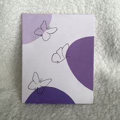 a purple and white square with two butterflies on the side, sitting on a fluffy surface