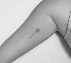 a small palm tree tattoo on the left arm and shoulder, with one single flower in it