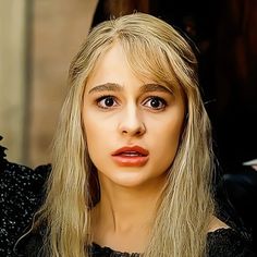 a woman with long blonde hair wearing a black dress and red lipstick looking at the camera