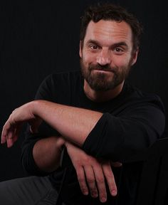 a bearded man sitting in a chair with his arms crossed and looking at the camera