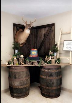 a deer head mounted on the wall above two wooden barrels filled with food and decorations