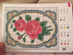 a cross stitch pattern with three roses in the center and leaves on each side, sitting on a table