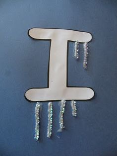 the letter t is made out of plastic beads and hangs on a blue wall with beaded chains