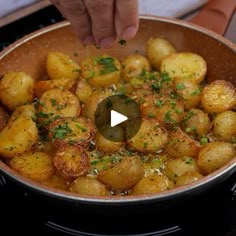 a pan filled with potatoes on top of a stove next to a person's hand