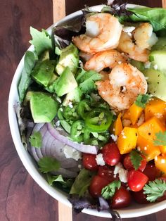 a salad with shrimp, lettuce, tomatoes and avocado in it