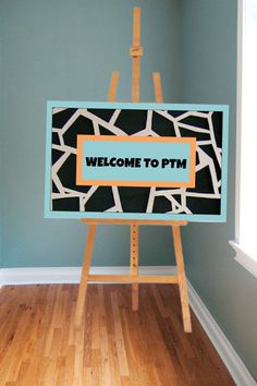 an easel with a welcome to ptm sign on it in front of a blue wall