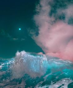 an ocean wave with pink and blue clouds in the sky, as seen from below