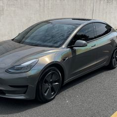 a silver electric car parked in front of a concrete wall on the side of a road