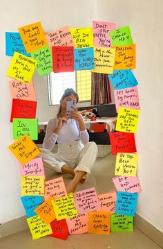 a woman sitting on the floor in front of a mirror covered in post it notes