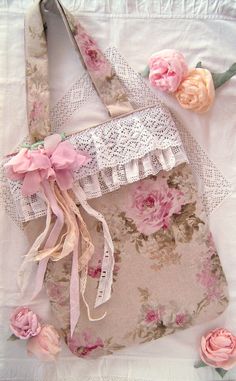 an old purse with pink flowers and lace on the bottom is laying on a white sheet