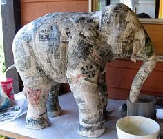 an elephant made out of newspaper sitting on top of a table next to a window