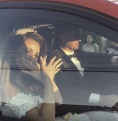 the bride and groom are sitting in their wedding car waving at each other's guests