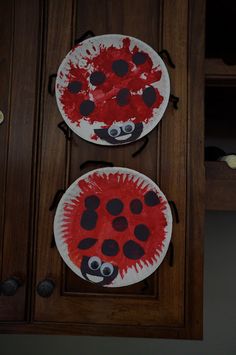 two paper plates with red and black designs on them sitting on a wooden cabinet door