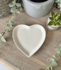 a white heart shaped plate sitting on top of a wooden table next to potted plants