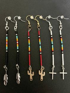 four different colored beads and cross charms on a black surface with one bead hanging from the side