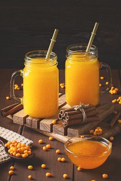 two mason jars filled with orange juice on top of a wooden table next to cinnamon sticks