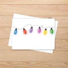 a card with christmas lights hanging from it's string on a wooden table next to a pair of scissors