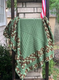 a green and brown blanket sitting on top of a wooden chair next to a brick wall