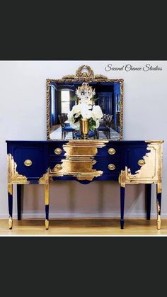 an ornate blue and gold dresser with flowers on the top, in front of a mirror