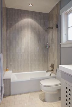 a white toilet sitting next to a bath tub in a bathroom with tile walls and floor