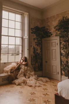 a woman sitting on the floor in front of a window with her hair blowing in the wind