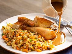 a white plate topped with corn, meat and gravy on top of a wooden table