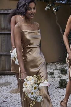 two women in gold dresses standing next to each other with flowers on their bouquets