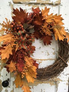 a wreath with autumn leaves and berries hanging on a white door frame in front of a brick wall