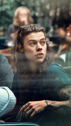 a man with long hair and glasses sitting in front of a glass window looking at the camera