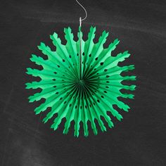 a green paper fan hanging from a string on a black background with space for text