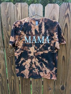 a tie dye shirt with the word mama on it hanging up against a wooden fence