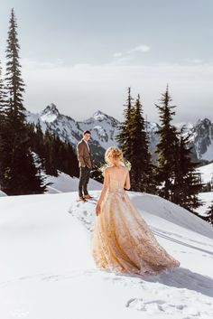 a bride and groom walking in the snow on top of a mountain with pine trees