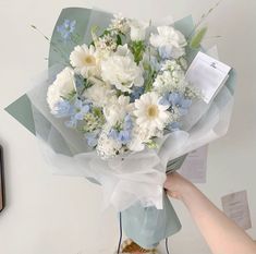 a bouquet of white and blue flowers is being held by a woman's hand