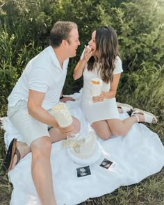 a man and woman sitting on a blanket eating cake