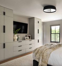 a bedroom with white furniture and a flat screen tv mounted on the wall above it