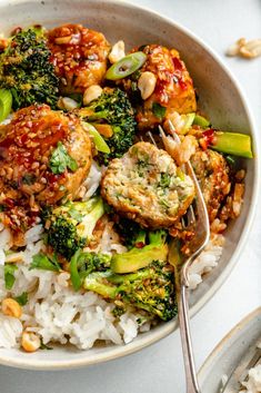 a white bowl filled with rice, broccoli and meatballs next to a fork