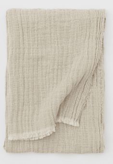 the textured linen blanket is folded on top of an unmade tablecloth with fringes