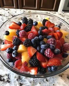 a glass bowl filled with fruit on top of a marble counter