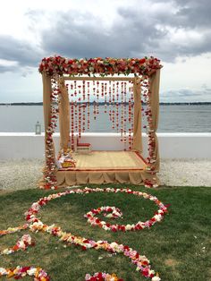 an outdoor ceremony set up with flowers and garlands on the grass by the water