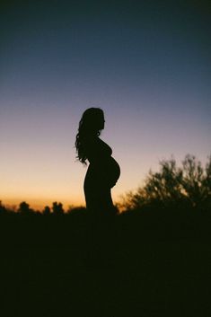 the silhouette of a pregnant woman in front of a purple and blue sky at sunset