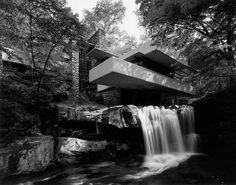 a waterfall in front of a modern house surrounded by trees and rocks with the water running under it