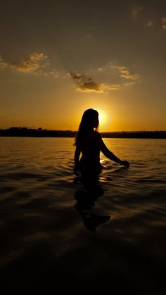 a woman is sitting in the water at sunset